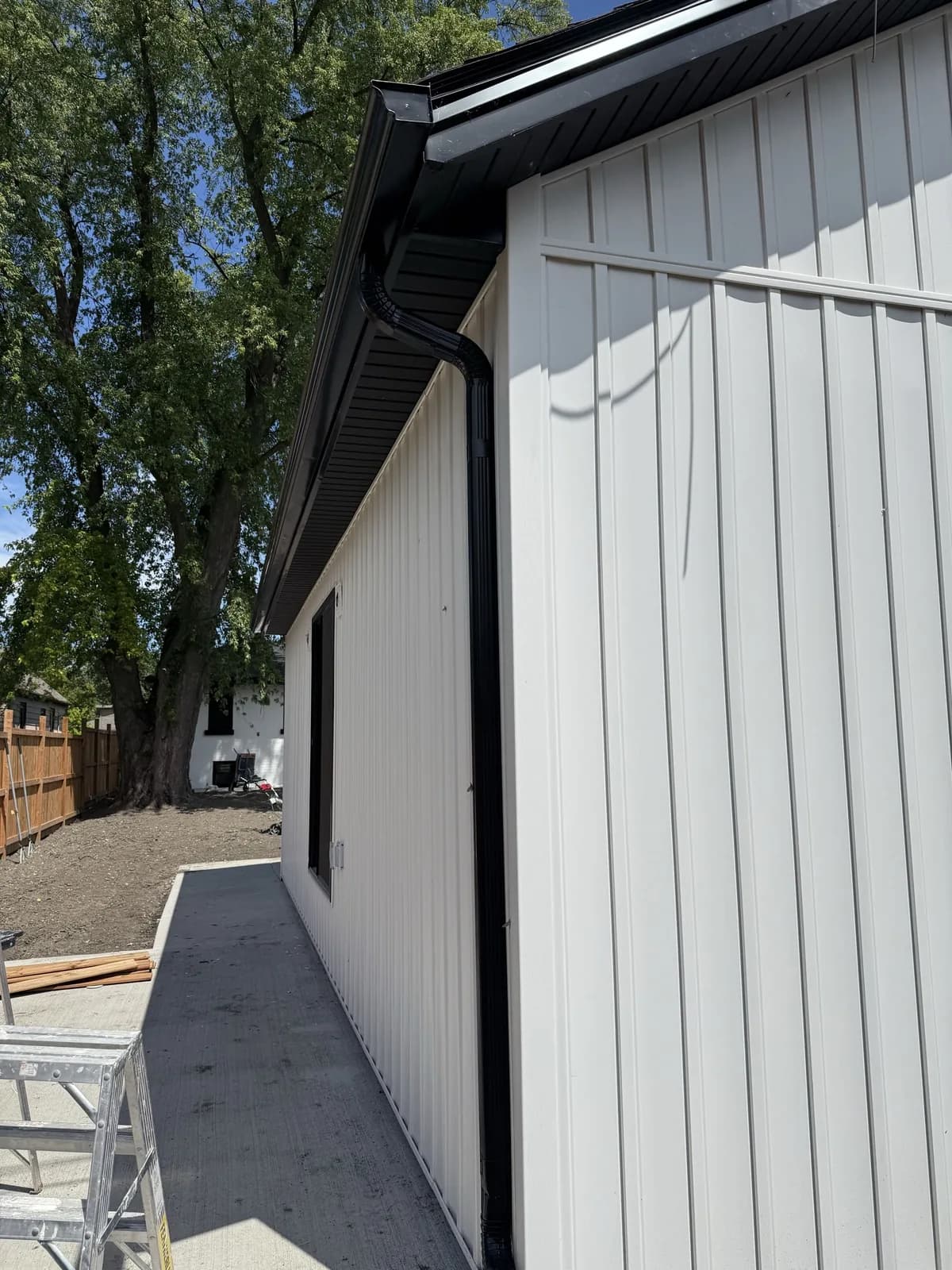 Dark eavestrough and downspout beside white vertical siding