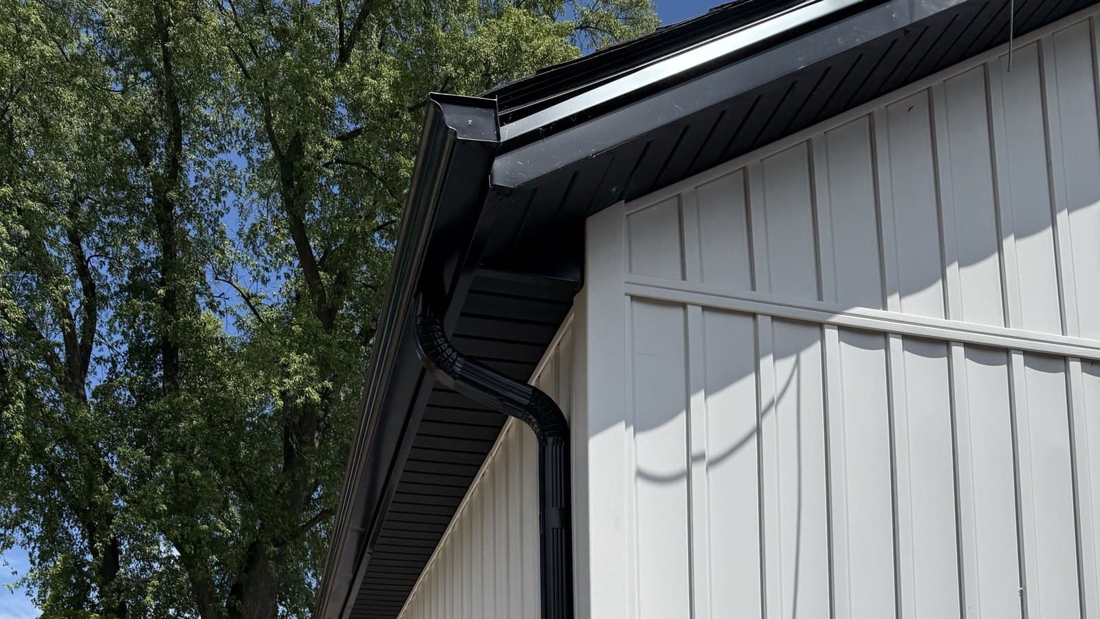 Dark eavestrough and downspout beside white vertical siding